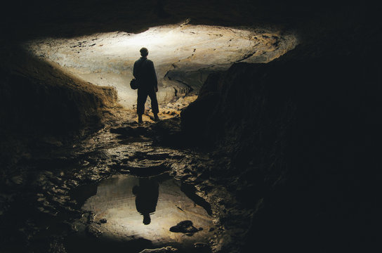 Man Silhouette Reflecting In Water In Dark Cave