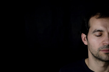 peaceful young man with closed eyes, black background