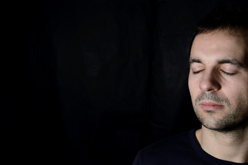 peaceful young man with closed eyes, black background
