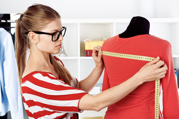 Young female stylist measuring dress on mannequin with tape.