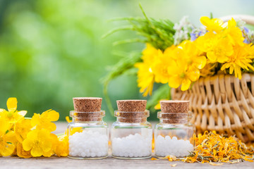 Bottles of homeopathy globules and healthy herbs in wicker baske