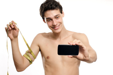 Skinny man taking a selfie with his phone while measuring his biceps with a centimeter. Beautiful teenager taking a photo for facebook.Anorexic young man training to become stronger
