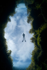 A freediver floats in freshwater under a cloud background over a chasm at Piccaninnie Ponds in...