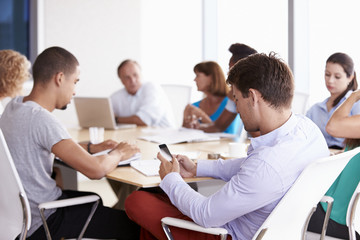Businessman Using Mobile Phone In Boardroom Meeting