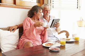 Obraz na płótnie Canvas Mature Couple Sitting At Breakfast Table With Digital Tablet