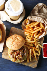 Tasty burger and french fries on plate, on wooden table background. Unhealthy food concept