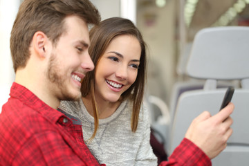 Couple of passengers sharing a smart phone inside a train
