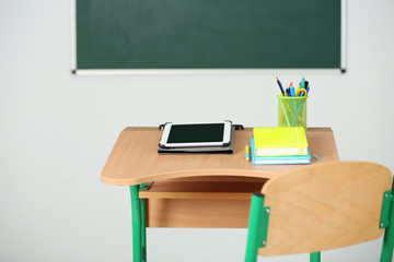 Wooden desk with stationery and tablet in class on blackboard background