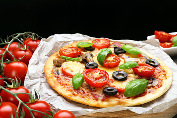Tasty pizza with vegetables and basil on black background
