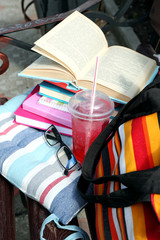 Books, glasses, drink and bag on bench outdoors