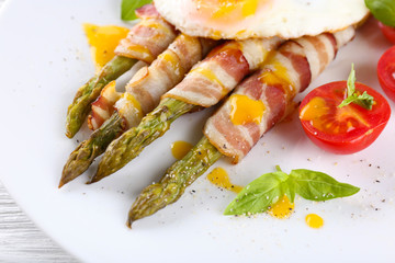 Dish of asparagus with bacon and egg in plate on table, closeup