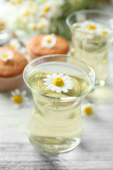 Obraz na płótnie Canvas Glass of chamomile tea with chamomile flowers and tasty muffins on color wooden background