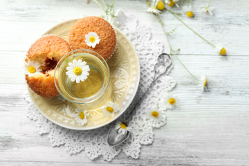 Glass of chamomile tea with chamomile flowers and tasty muffins on color wooden background