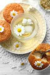Fototapeta na wymiar Glass of chamomile tea with chamomile flowers and tasty muffins on color wooden background