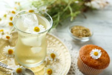Obraz na płótnie Canvas Glass of chamomile tea with chamomile flowers and tasty muffin on color wooden background