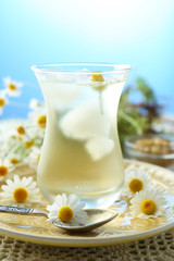 Glass of cold chamomile tea with ice cubes and chamomile flowers on table, on colorful background