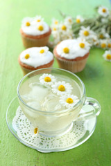 Obraz na płótnie Canvas Cup of chamomile tea with chamomile flowers and tasty muffins on color wooden background