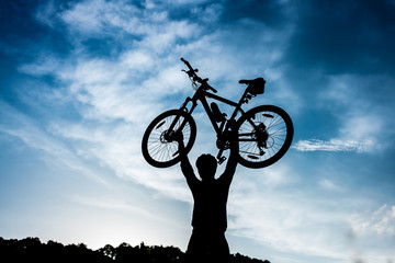 biker is holding bicycle above his head at sunrise.