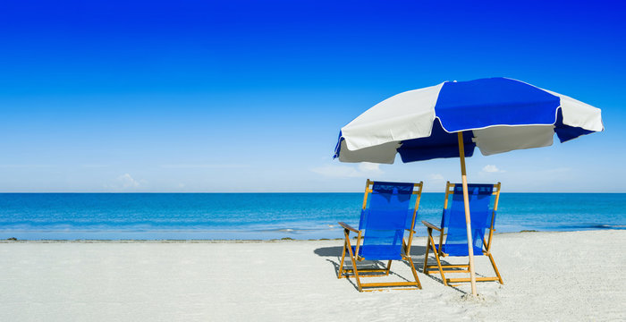 Fototapeta sun loungers and a beach umbrella on silver sand,  vacation conc