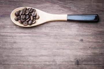 Coffee beans on spoon and wooden background