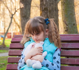 Angry, dissatisfied little girl with  toy on  park bench