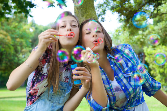 Happy blonde sisters having fun blowing soap bubbles in park
