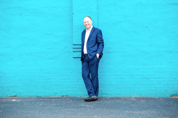 Positive businessman leaning on turquoise wall