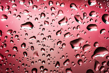 Water drops on glass with red background.