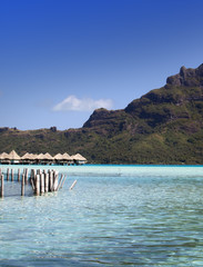 the destroyed thrown huts on water and island with palm trees in the ocean and mountains on a background..