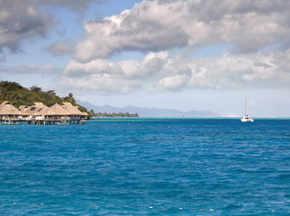 Typical Polynesian landscape - seacoast with palm trees and small houses on water.