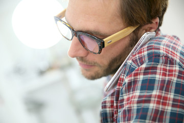 Trendy guy with eyeglasses talking on phone in office