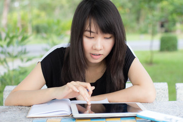 Portrait of thai student teen beautiful girl using her tablet sitting in park.