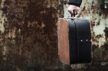 Ancient suitcase in a hand on rusty grunge a background.  Old suitcases.