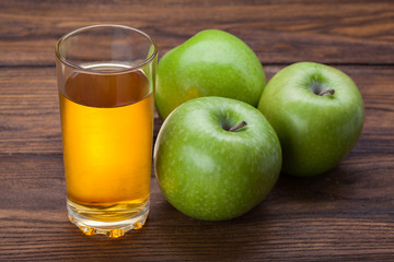 Glass of apple juice and apples on wood
