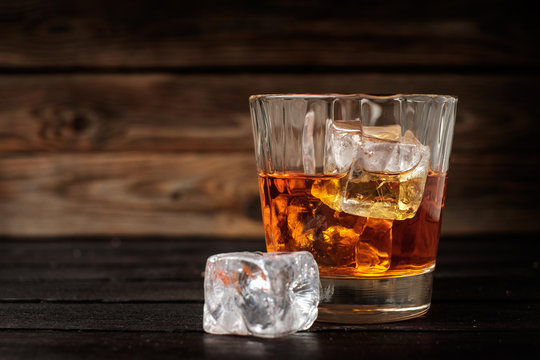 Glass of whiskey with ice on a wooden background.