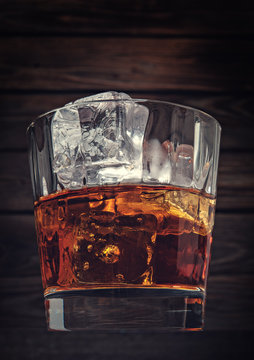 Glass of whiskey with ice on a wooden background made with vinta