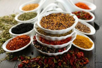 Different kinds of spices in ceramics spoons, close-up, on wooden background
