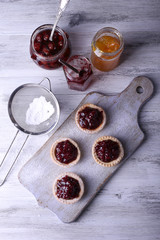 Delicious cookies with jam and powdered sugar on cutting board on wooden background