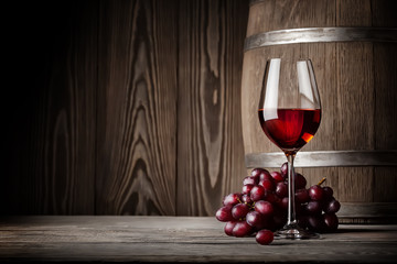 Glass of red wine with grapes and barrel