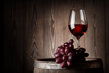 Glass of red wine with grapes on wooden barrel