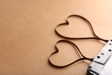 Audio cassette with magnetic tape in shape of hearts on brown background