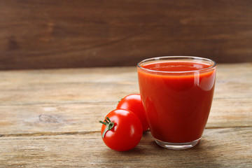 Glass of fresh tomato juice on wooden background