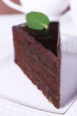 Piece of chocolate cake with mint on white plate, closeup
