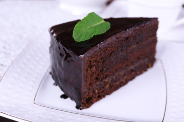 Piece of chocolate cake with mint on white plate, closeup