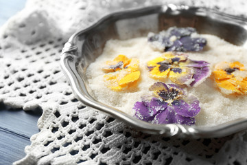 Candied sugared violet flowers on tray, on color wooden background
