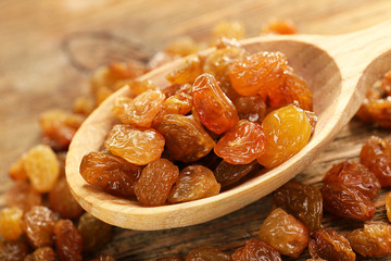 Raisins in spoon on wooden table, closeup