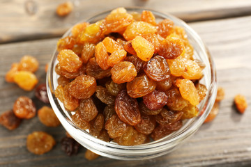 Raisins in glass saucer on wooden table, closeup