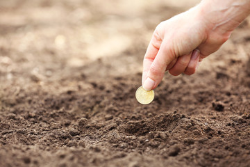 Female hand planting coin into soil, outdoors