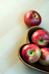 Apples in the wooden heart shape plate on the table, close up