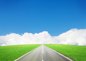 Fototapeta premium Asphalt road through the green field and blue sky
